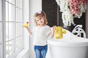 Funny little baby girl with curly hair. Get ready to take a bath. Spacious lighted bathroom. The concept of a healthy and clean body. Caring for yourself since childhood photo