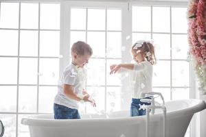 niño jugando con pétalos de rosa en el baño de su casa. niña y niño adulando diversión y alegría juntos. el concepto de infancia y la realización de sueños, fantasía, imaginación foto