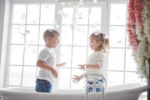 niño jugando con pétalos de rosa en el baño de su casa. niña y niño adulando diversión y alegría juntos. el concepto de infancia y la realización de sueños, fantasía, imaginación foto