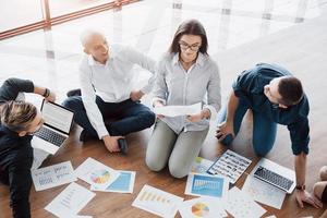 jóvenes creativos en la oficina moderna. grupo de jóvenes empresarios están trabajando junto con la computadora portátil. autónomos sentados en el suelo. logro corporativo de cooperación. concepto de trabajo en equipo foto