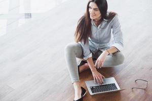 Side view of attractive girl using a laptop in public wifi area and smiling while sitting on the floor photo