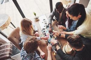 Top view creative photo of friends sitting at wooden table. Friends having fun while playing board game