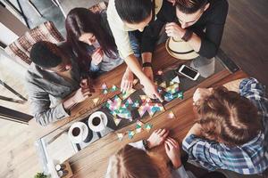 Top view creative photo of friends sitting at wooden table. Friends having fun while playing board game