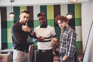 Prometedores jóvenes multiétnicos celebrando y bebiendo tostadas de whisky, reloj gadget foto
