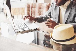 pensativo afroamericano guapo escritor profesional de artículos populares en un blog vestido con un atuendo moderno y gafas pensando en una nueva historia revisando su guión desde un cuaderno sentado en la cafetería foto