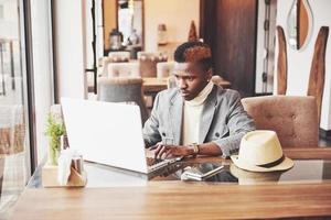 Retrato de hombre afroamericano sentado en un café y trabajando en un portátil. foto