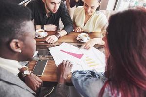 concepto de reunión de lluvia de ideas de trabajo en equipo de diversidad de inicio. Compañeros de trabajo del equipo de negocios que comparten el documento del informe de la economía mundial portátil. foto