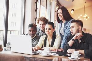 Gente de negocios multiétnica, emprendedor, negocio, concepto de pequeña empresa, mujer mostrando algo a sus compañeros de trabajo en una computadora portátil mientras se reúnen alrededor de una mesa de conferencias foto