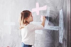 dibujo de niña rizada con crayón de color en la pared. obras de niño. lindo alumno escribiendo en la pizarra foto