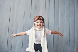 Beautiful smiling child in helmet on a blue background playing with a plane. Vintage pilot concept photo