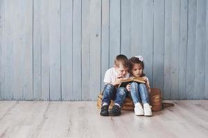 Ready to big travel. Happy little girl and boy reading interesting book carrying a big briefcase and smiling. Travel, freedom and imagination concept photo