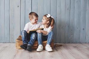 listo para grandes viajes. feliz niña y niño leyendo un libro interesante con un maletín grande y sonriendo. concepto de viaje, libertad e imaginación. foto