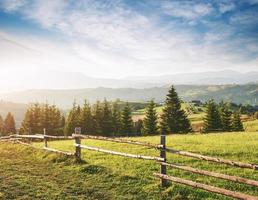 Beautiful summer mountain landscape at sunshine. View of the meadow fenced fence. Rural landscape