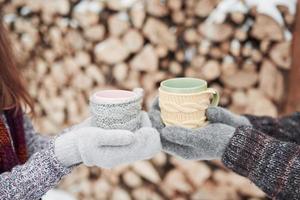 Couple hands in mittens take a mugs with hot tea in winter park photo