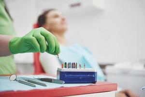 un paciente en una clínica dental se sienta en una silla y el médico prepara las herramientas para el tratamiento foto