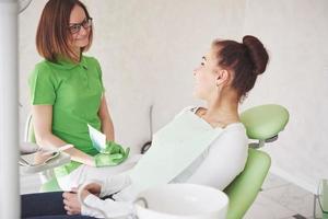 Female dentist in dental office talking with female patient and preparing for treatment photo
