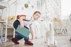 Cute little boy is going to school for the first time. Child with school bag and book. Kid makes a briefcase, child room on a background. Back to school photo