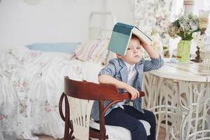 Photo of diligent schoolboy with book on his head doing homework. The schoolboy is tired of doing homework
