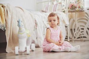 Beautiful little girl playing toys. Blue-eyed blonde. White chair. Children's room. Happy small girl portrait. Childhood concept photo