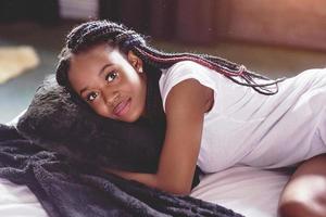 una hermosa mujer africana yace y duerme en la cama, en un dormitorio blanco. buenos dias vacaciones en casa. la niña lleva una camiseta, coletas en la cabeza foto