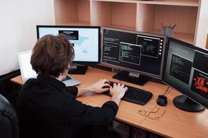 el joven y peligroso pirata informático destruye los servicios gubernamentales al descargar datos confidenciales y activar virus. un hombre usa una computadora portátil con muchos monitores