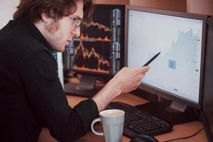 Stressful day at the office. Young businessman holding hands on his face while sitting at the desk in creative office. Stock Exchange Trading Forex Finance Graphic Concept photo