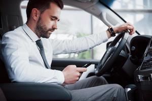 Hombre de negocios joven satisfecho mirando el teléfono móvil mientras conduce un coche foto