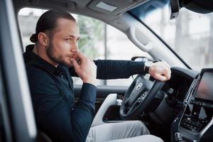 Confiado joven empresario sentado al volante de su coche nuevo