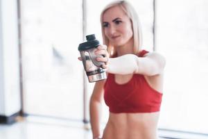 Foto de atractiva mujer fitness en el gimnasio y sosteniendo una botella de agua