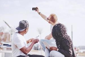 Hermosos amigos multiétnicos usando una computadora portátil en la calle y hacen selphie. concepto de estilo de vida juvenil foto