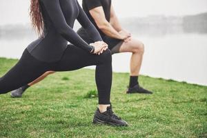 Fitness couple stretching outdoors in park near the water. Young bearded man and woman exercising together in morning photo