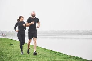 Couple jogging and running outdoors in park near the water. Young bearded man and woman exercising together in morning photo