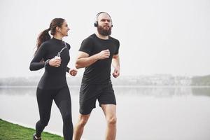 Couple jogging and running outdoors in park near the water. Young bearded man and woman exercising together in morning photo