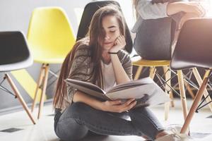 Two beautiful twin girls spend time read a book in library in the morning. Sisters relaxing in a cafe and having fun together photo