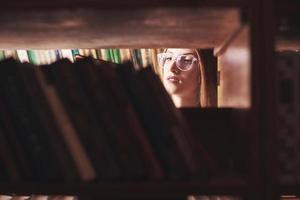 una joven estudiante busca el libro adecuado en los estantes de la antigua biblioteca universitaria foto
