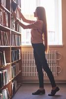 A young student girl is looking for the right book on the shelves of the old university library photo