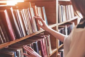 Joven y atractiva bibliotecaria estudiante leyendo un libro entre las estanterías de la biblioteca foto