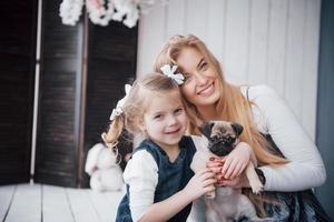 Happy loving family. Mother and her daughter child girl playing and hugging adorable pug photo