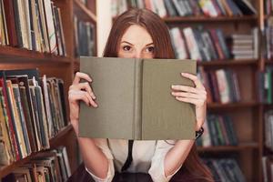 Young attractive student librarian reading a book between library bookshelves photo