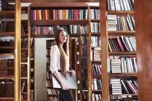 Young beautiful woman is a student at a library with her laptop photo