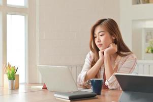 Asian female student intently reading the laptop. She is preparing for the exam to graduate. photo