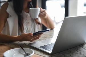 mujeres empresarias están tomando café y usando teléfonos inteligentes. ella trabaja entre el freno de café, la computadora portátil sobre el escritorio. foto