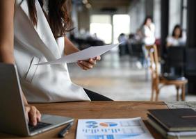 Female executive hold the data graph in hand and are using a laptop. She sat on the desk in office. photo