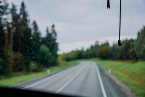 gota de agua de lluvia en la ventana. vista de la carretera y el bosque de otoño foto