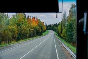 View of the road and the autumn forest through the bus window. Road trip photo