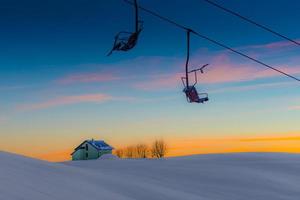 Old chair lift on ski slopes abandoned, with the colors of tsunset and Alpine chalet photo