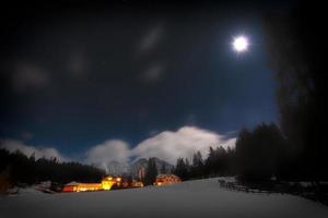 casas en la nieve en una noche estrellada con la luna foto