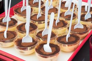 Close up of a tray with tiramisu in small bowls, with a spoon in each of them photo