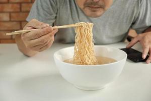 Hungry casual Thai man use chopsticks to eat hot instant noodles in white cup during lunch breaks, quick, tasty, and cheap. Traditional healthy Asian fast food meal of Japanese and Chinese lifestyle. photo