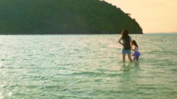 Blur-Focused VDO. A mother took her daughter's hand for a walk in the sea with love in the evening. While there are orange lights and sunsets on a beach in the summer during the kid's vacation. video